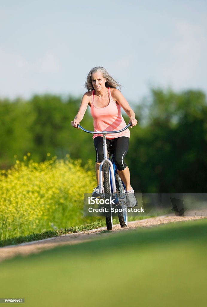 Senior donna in bicicletta di equitazione - Foto stock royalty-free di Fiore di campo