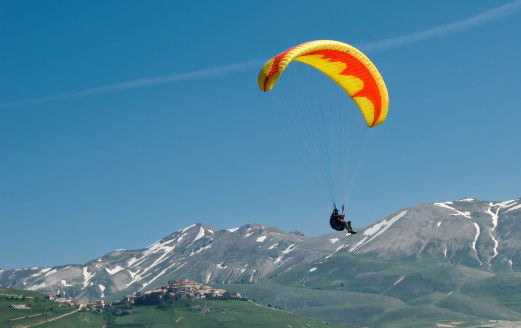 A paraglider soars over the mountain village of Castelluccio in the Piano Grande, Italy