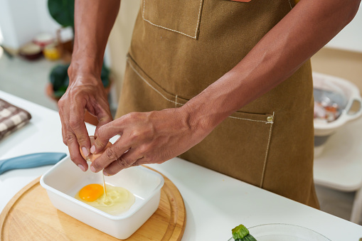 Close-up of Asian man's hands cracking fresh eggs Try it in boxed container. to prepare an omelet for breakfast Before going to work, a lot of bread and eggs lay on table. along with fresh vegetables