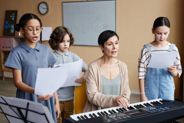 Children singing songs together with teacher Group of children singing songs together with teacher while she playing piano during music lesson school choir stock pictures, royalty-free photos & images