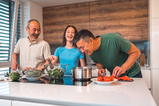 Multigenerational Asian family members standing in a domestic kitchen preparing a meal together. Spending quality time together cooking.