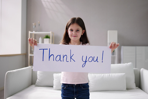Close-up Of A Smiling Girl Holding Thank You Sign Against White Background