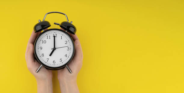 istock Woman's hands holding a black alarm clock on a yellow background 1490711983