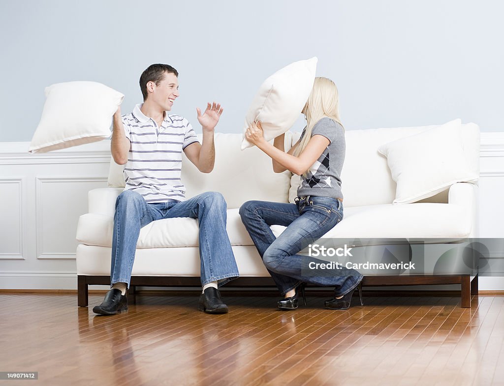 Casal jovem tendo uma briga de travesseiro em sofá - Foto de stock de Briga de Travesseiro royalty-free