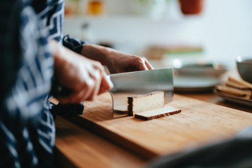 Close up shot of an anonymous woman taking cut slices of tofu cheese and putting them on a plate for making a meal at home.