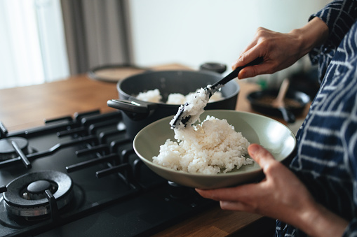 Close up shot of an unrecognizable woman filling a bowl with cooked rice in the kitchen  at home.