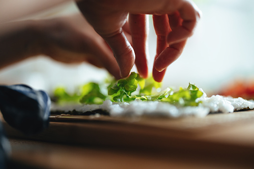 Close up shot of woman's hands placing lettuce on rice for a homemade sushi.