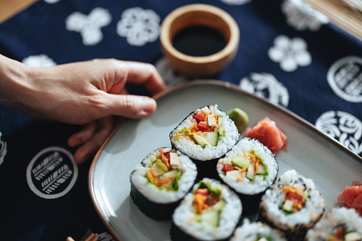 Close up of an anonymous woman holding a plate with vegetable sushi dish. They are nicely arranged on the plate.