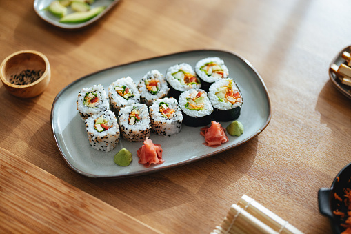 Close up on a plate with arranged sessame seed and seaweed sushi rolls placed on a wooden table.