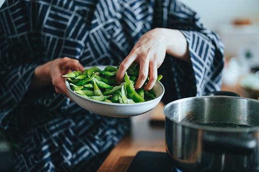 Close up of an unrecognizable woman grabbing a handful of green beans so she can add them to a cooking pot.