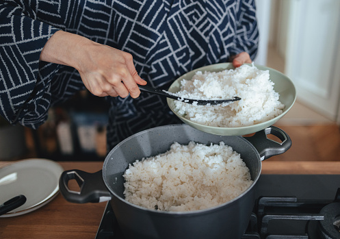 Close up shot of an unrecognizable woman filling a bowl with cooked rice in the kitchen  at home.