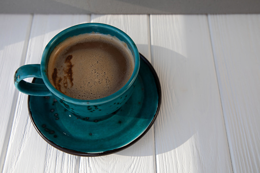 Blue mug with coffee, cappuccino, tea on a white wooden table with shadows. Top view, close-up