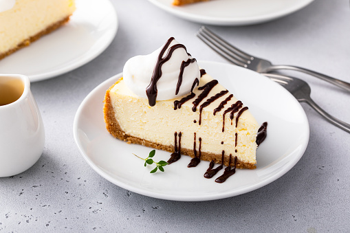 Slice of a traditional New York cheesecake with dollop whipped cream and chocolate sauce