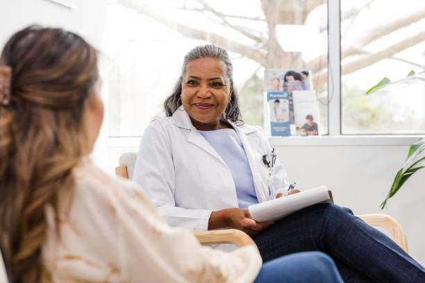 Senior adult female psychiatrist smiles while listening to female patient stock photo