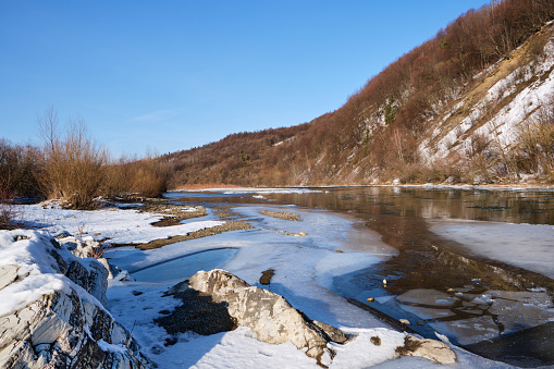 A view of a mountain river with ice and mountains covered with snow and stones with different structures and a clear sky