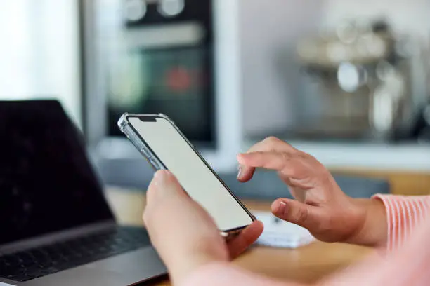 A woman using a smartphone with an empty white screen, sitting in front of the turned-off laptop.