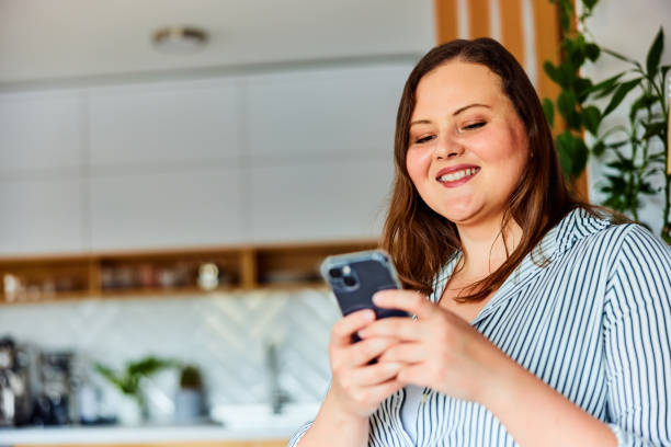 istock A close-up of a smiling plus-size woman using her mobile phone at home. 1490720907