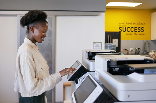 Young Black woman uses photocopier machine in shared office workspace. High quality photo