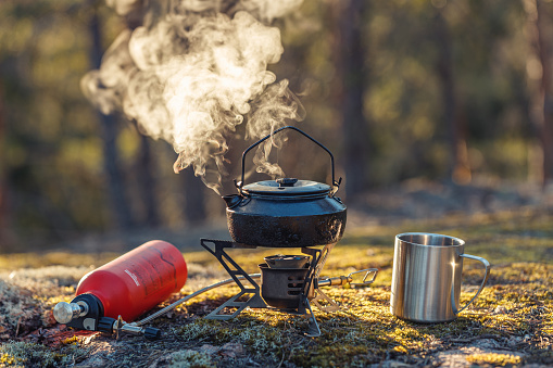 Boiling kettle on a multifuel burner with a mug in the forest.