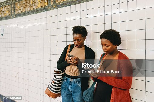 istock Two friends are using smart phones against a white tiles wall 1490736350
