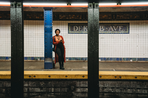 A woman is waiting for the train in Dekalb Ave station in Brooklyn. She's standing, holding her smart phone.