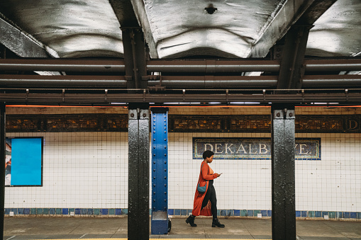 A woman is walking in Dekalb Ave station in Brooklyn. She's walking, holding her smart phone.