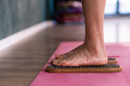 Standing barefoot woman doing nail reflexotherapy at professional yoga class feet of female person on sadhu boards on pink mat in spacious studio effective body relaxation practice closeup