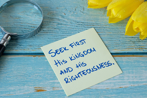 Seek first His kingdom and righteousness, handwritten biblical verse on a note with magnifying glass and yellow tulips on wood. A closeup. Christian change, obedience to God Jesus Christ concept.