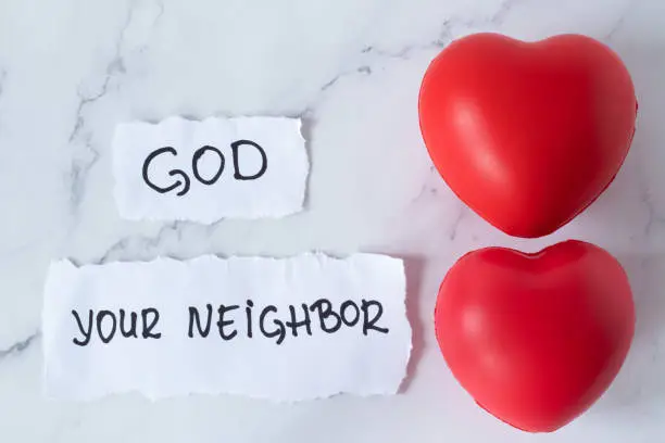 Love God and your neighbor, handwriting on paper with two red hearts on white marble table. Top view. The greatest commandment, obedience to God Jesus Christ, Christian biblical Law concept.