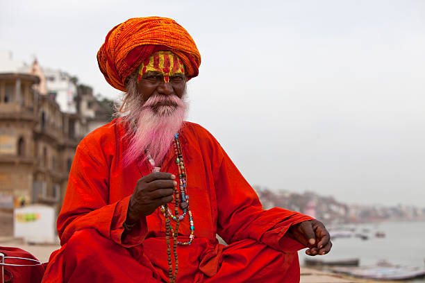 Holy Indian Sadhu wearing an orange turban with a red robe Sadhu at the ghats in Varanasi, India.  varanasi stock pictures, royalty-free photos & images
