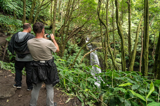 Two men photographing the waterfall Salto De Prago in rain forest in Faial da Terra, Sao Miguel island in Azores