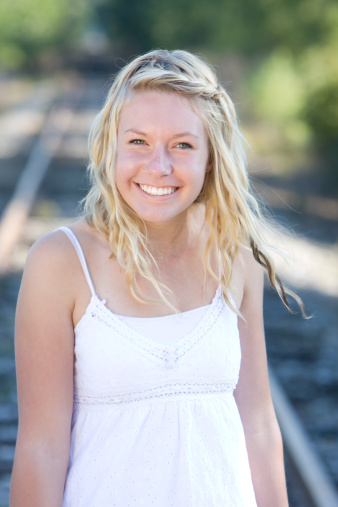 pretty blond teenager on the railroad tracks smiling with windblown hair