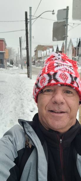 Face of a middle-aged man with a red cap on his head walking down the street full of snow and parked cars