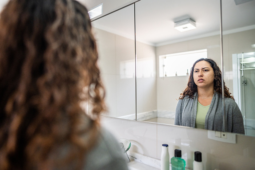 Young woman looking at herself in mirror in bathroom at home