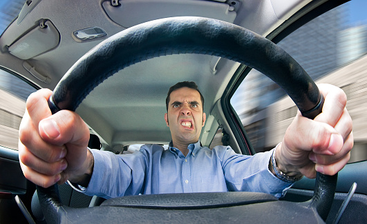 A furious man driving, as seen from behind the wheel. Shot using a very wide fisheye lens focused on the driver's face.