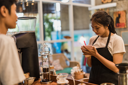 Photo captures the essence of a traditional Balinese coffee shop, where skilled individuals of Asian descent passionately prepare and serve coffee, creating a welcoming space for locals and tourists alike to indulge in the rich flavors and cultural experience of Balinese coffee culture.