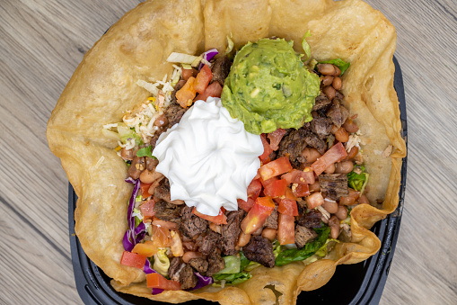 Overhead view of crispy tostada shell contains this generous fajita taco salad with large scoops of sour cream and guacamole on top.