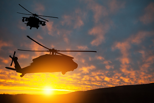 Silhouette of a military helicopter flying during sunset.