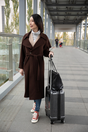 A businesswoman walking inside an airport terminal with carry-on luggage.