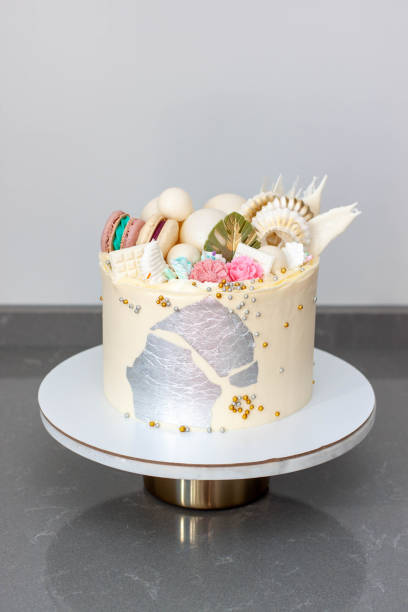 istock Modern elegant white cake with white chocolate, waffle paper, macaroons, edible silver and meringues. 1490762768