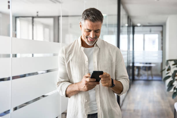 istock Smiling mature businessman holding and using smartphone applications in office. 1490764481