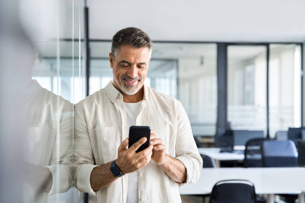 istock Smiling mature businessman holding and using smartphone applications in office. 1490764492