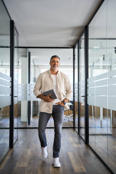 Senior businessman walking with digital tablet inside modern company office. stock photo