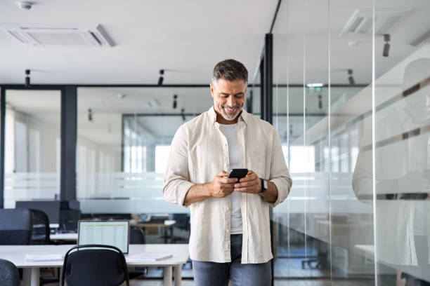 istock Smiling mature businessman holding and using smartphone applications in office. 1490764526