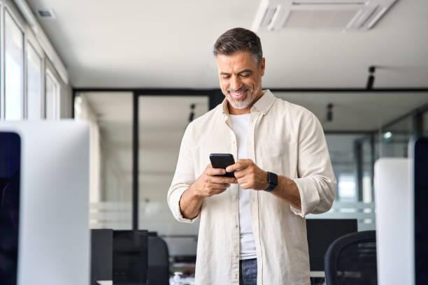 istock Smiling mature businessman holding and using smartphone applications in office. 1490764536