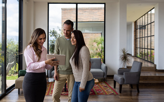 Real estate agent showing a house for sale to a couple and looking at the details on a tablet
