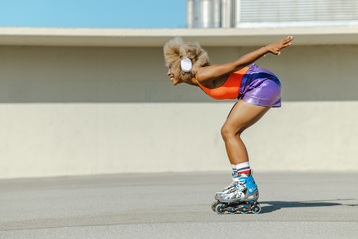 Side view of woman with afro hairstyle rollerblading on sunny promenade