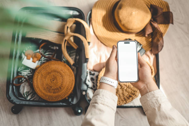 istock Mockup image of a woman's hands holding smart phone with blank white screen and hat on suitcase background 1490766668