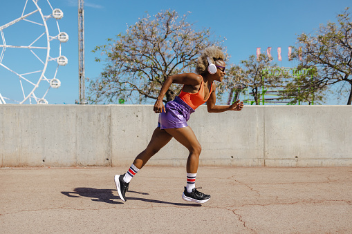 African American woman in a sports outfit running and enjoying a sunny day in the city