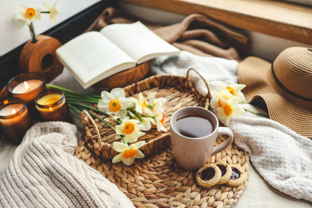 Spring still life, cup of tea, candles, open book and hat